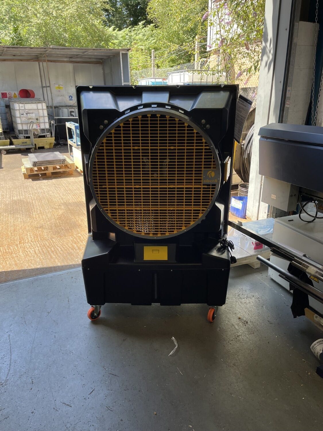 Large industrial fan with a yellow grille standing on wheels in a warehouse doorway.
