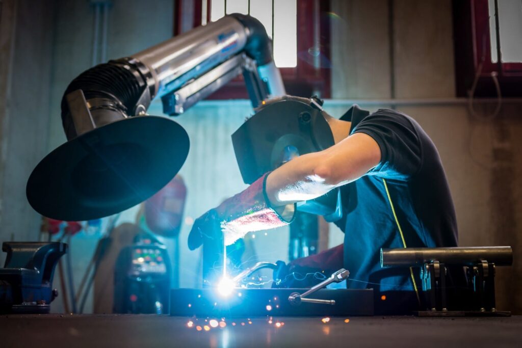 WhyMcCarthyHire A person welding metal, wearing protective gear, in an industrial workshop.